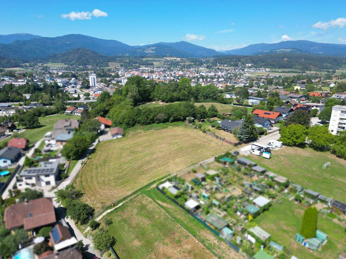 Luftaufnahme eines Baugrundstücks in einer Siedlung, angrenzend an Kleingärten und mit Stadtblick.