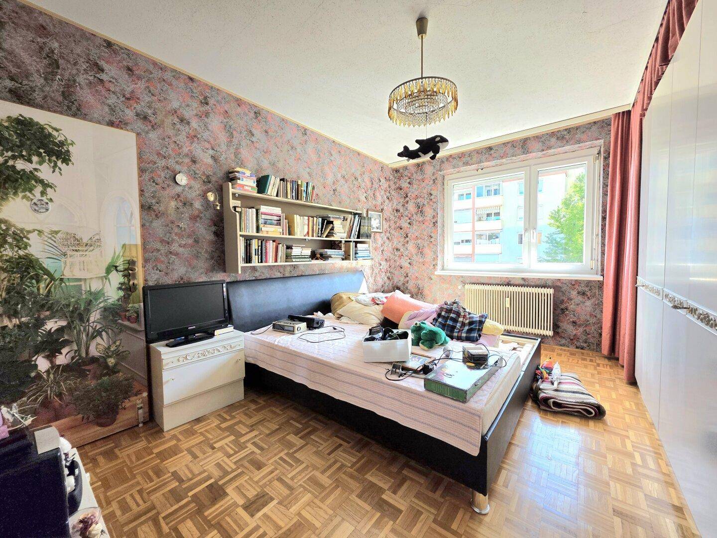 Schlafzimmer mit Parkettboden, gemusterter Tapete und großem Fenster.
