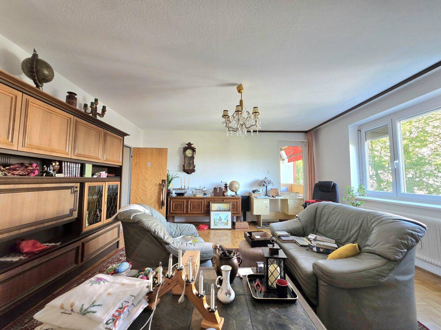 Helles Wohnzimmer mit Holzmöbeln, Parkettboden und Zugang zu einem weiteren Bereich.