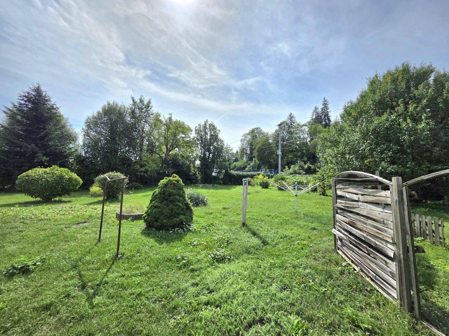 Großer, sonniger Garten mit Rasenfläche, Bäumen und einem Holzzaun im ländlichen Stil.
