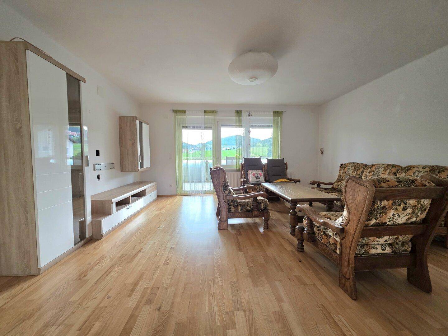Helles Wohnzimmer mit Holzboden, traditionellen Möbeln und Blick ins Grüne.