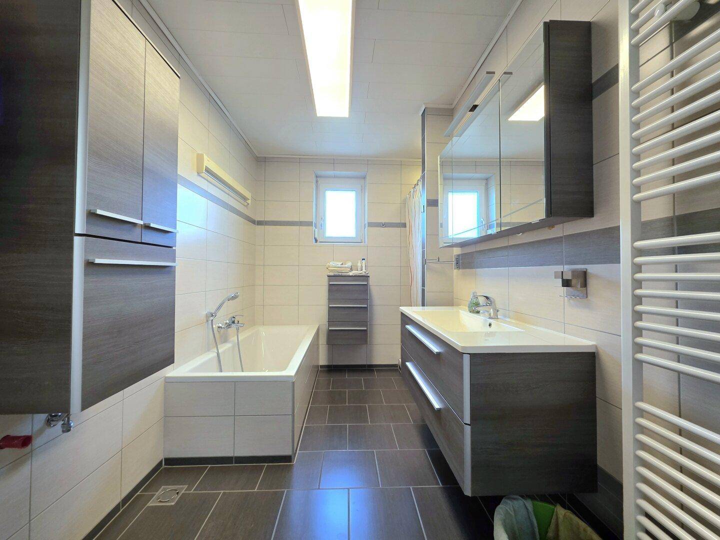 Modernes Badezimmer mit Badewanne, Doppelwaschbecken und dunklen Fliesen.