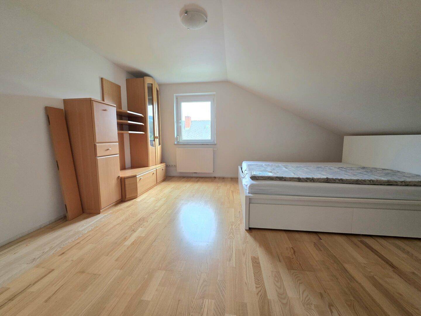 Schlafzimmer im Dachgeschoss mit Holzboden, Schräge und einfacher Einrichtung.