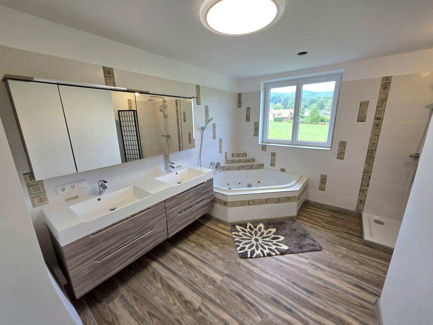 Großes Badezimmer mit Eckbadewanne, Doppelwaschbecken und Blick ins Grüne.