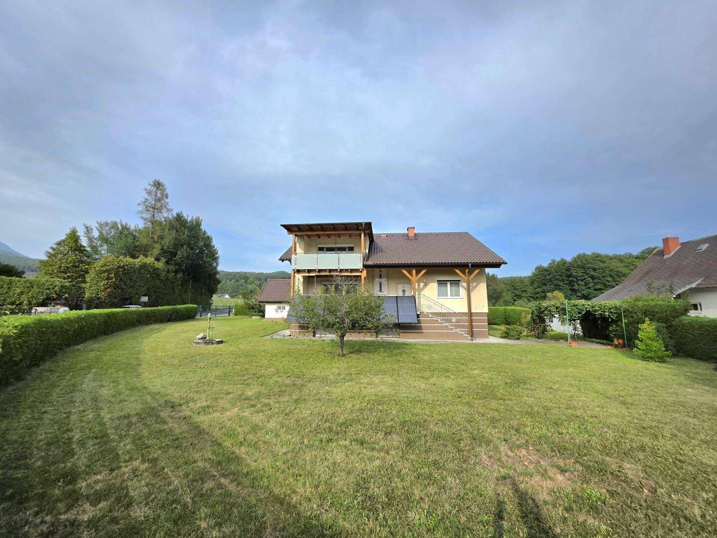 Freistehendes Haus mit großem Garten und ländlicher Umgebung unter bewölktem Himmel.