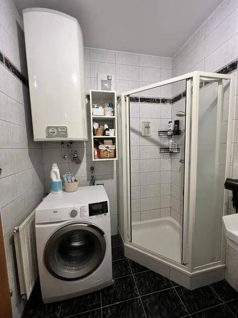 Badezimmer mit Duschkabine, Waschmaschine und Warmwasserboiler, praktisch eingerichtet.