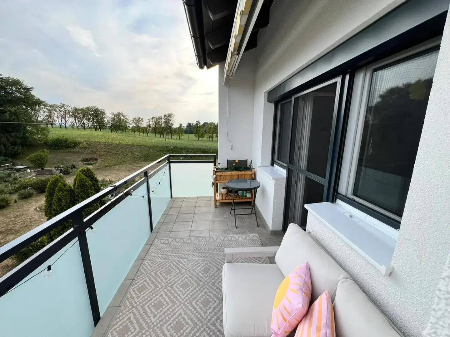 Möblierter Balkon mit Glasbrüstung und weitem Blick ins Grüne, ideal zum Entspannen.