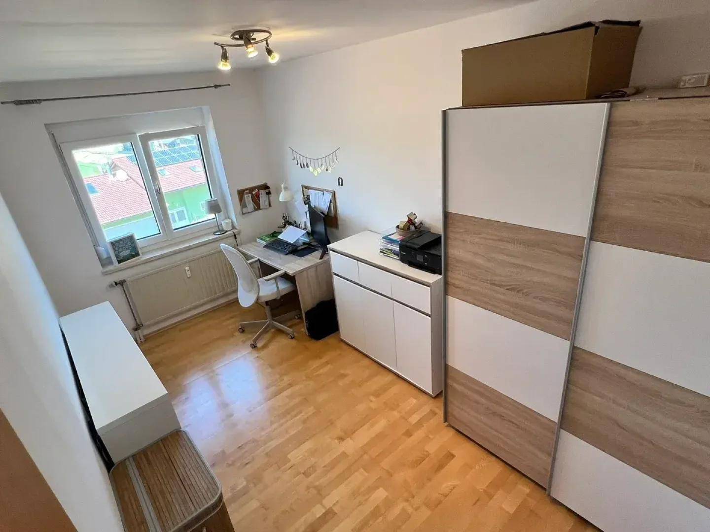 Helles Zimmer mit Holzboden, Schreibtisch und Kleiderschrank, ideal als Kinder- oder Arbeitszimmer.