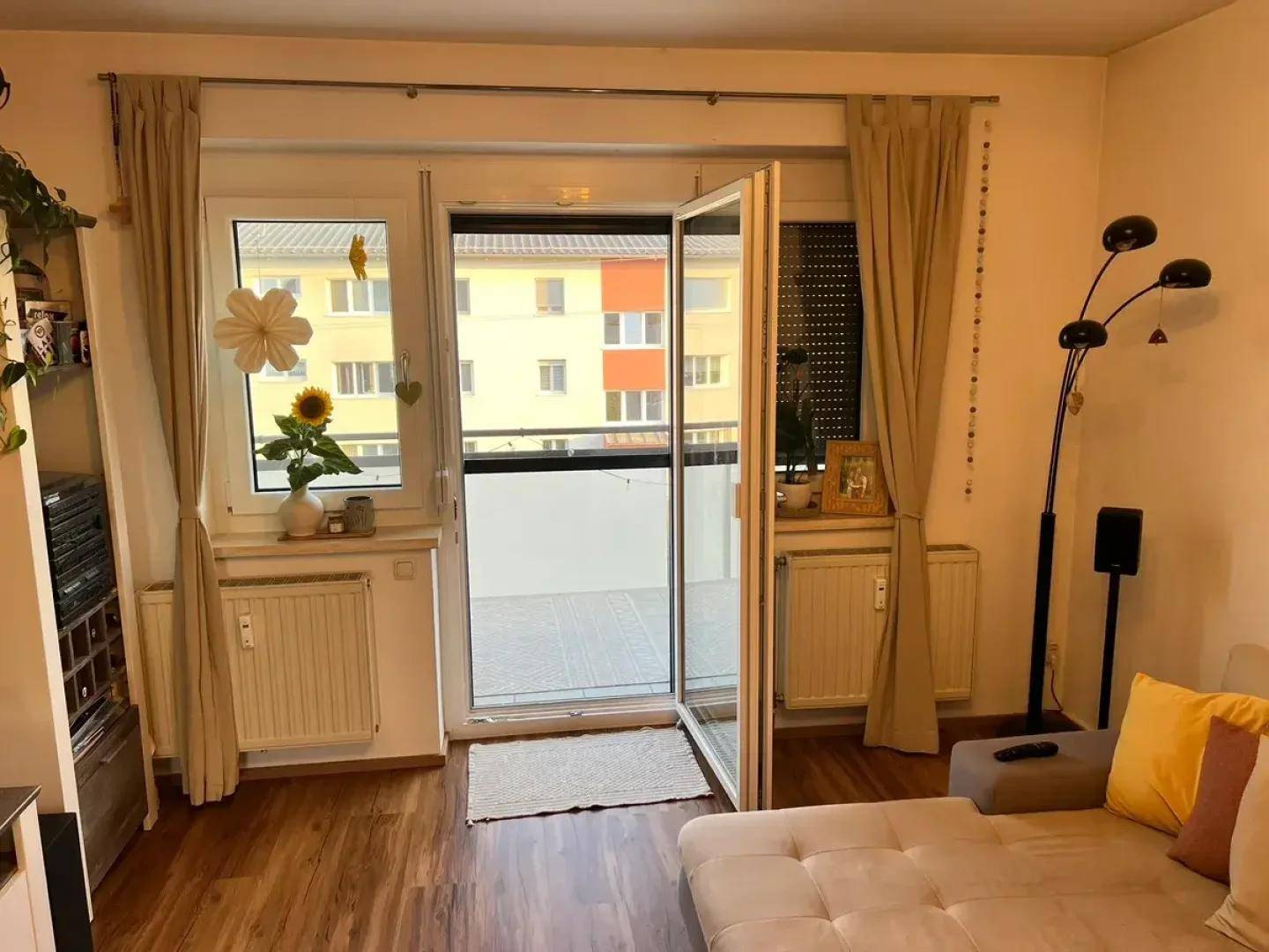 Wohnzimmer mit Balkonzugang und großen Fenstern, die viel Tageslicht hereinlassen.