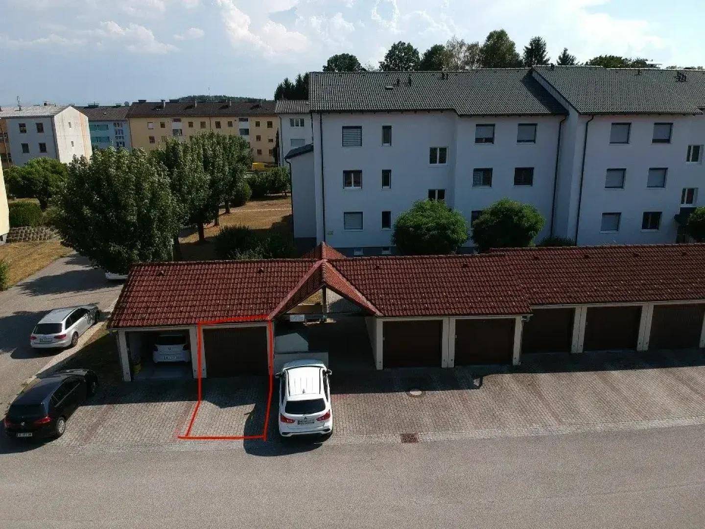 Reihe von Garagen und Carports neben einem Wohngebäude, mit einem markierten Stellplatz.