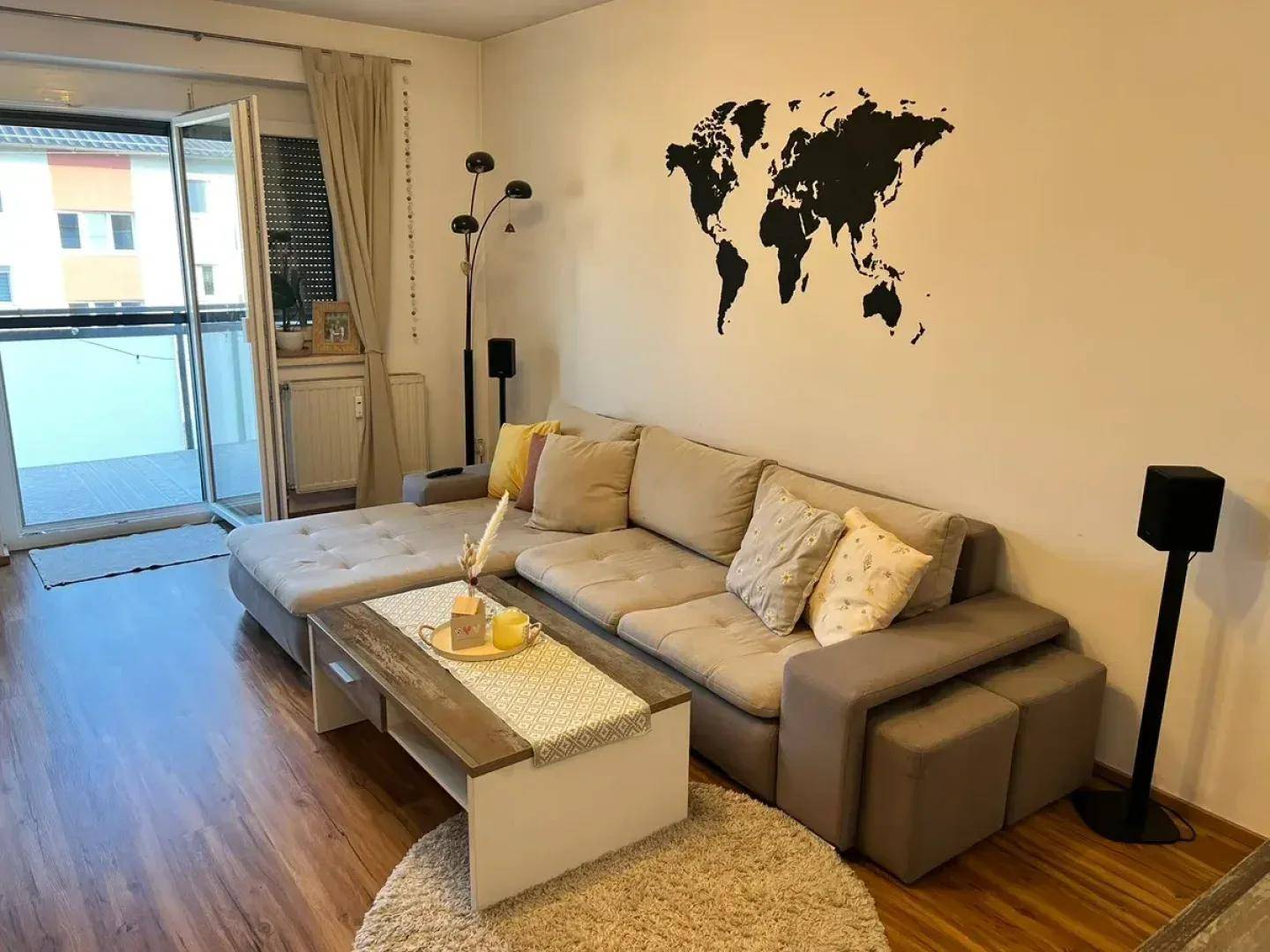 Gemütliches Wohnzimmer mit großem Ecksofa, Holzboden und Zugang zu einem Balkon.