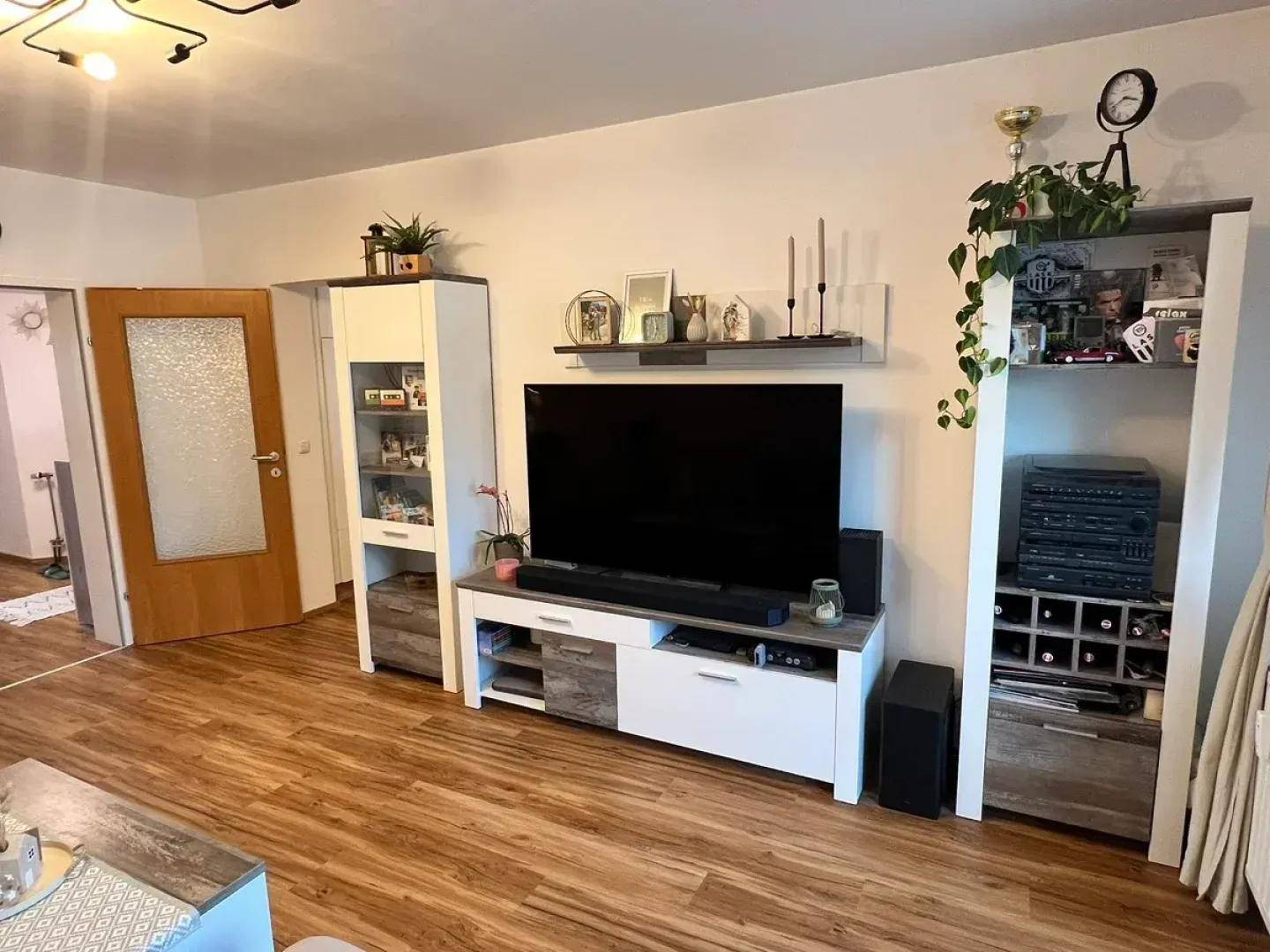 Wohnbereich mit TV-Möbeln, Regalen und durchgehendem Holzoptikboden.