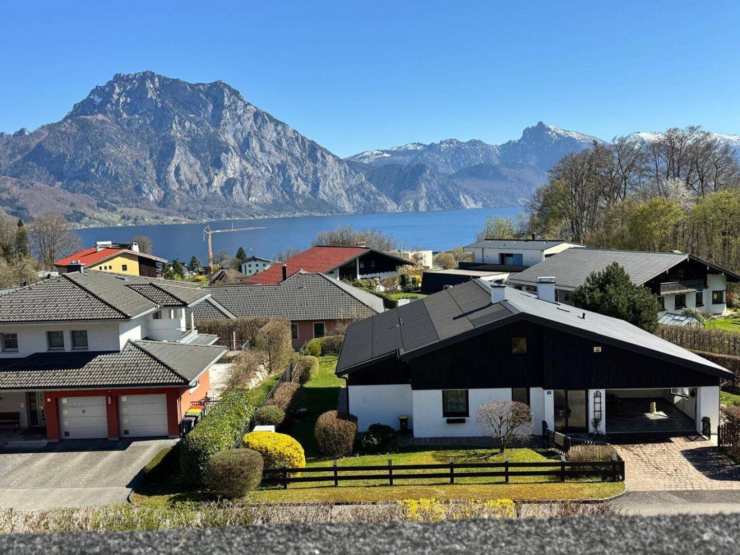 Panoramablick auf Häuser, See und majestätische Berge unter blauem Himmel.