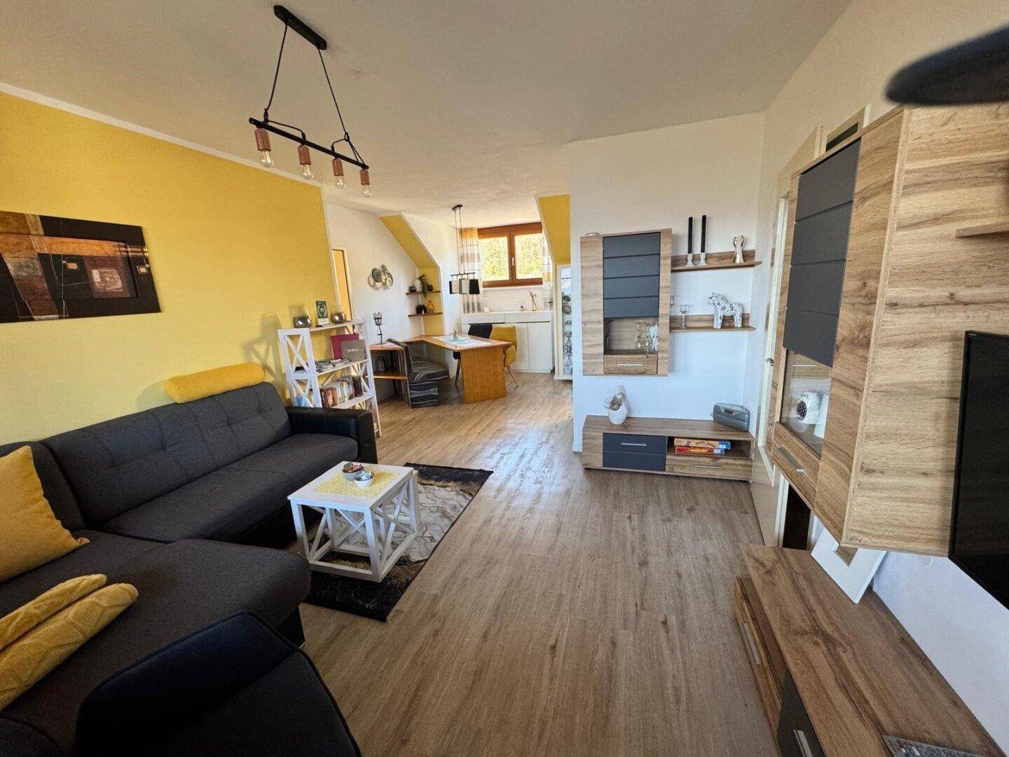 Offener Wohn- und Essbereich mit Laminatboden, gelben Akzentwänden und moderner Einrichtung.