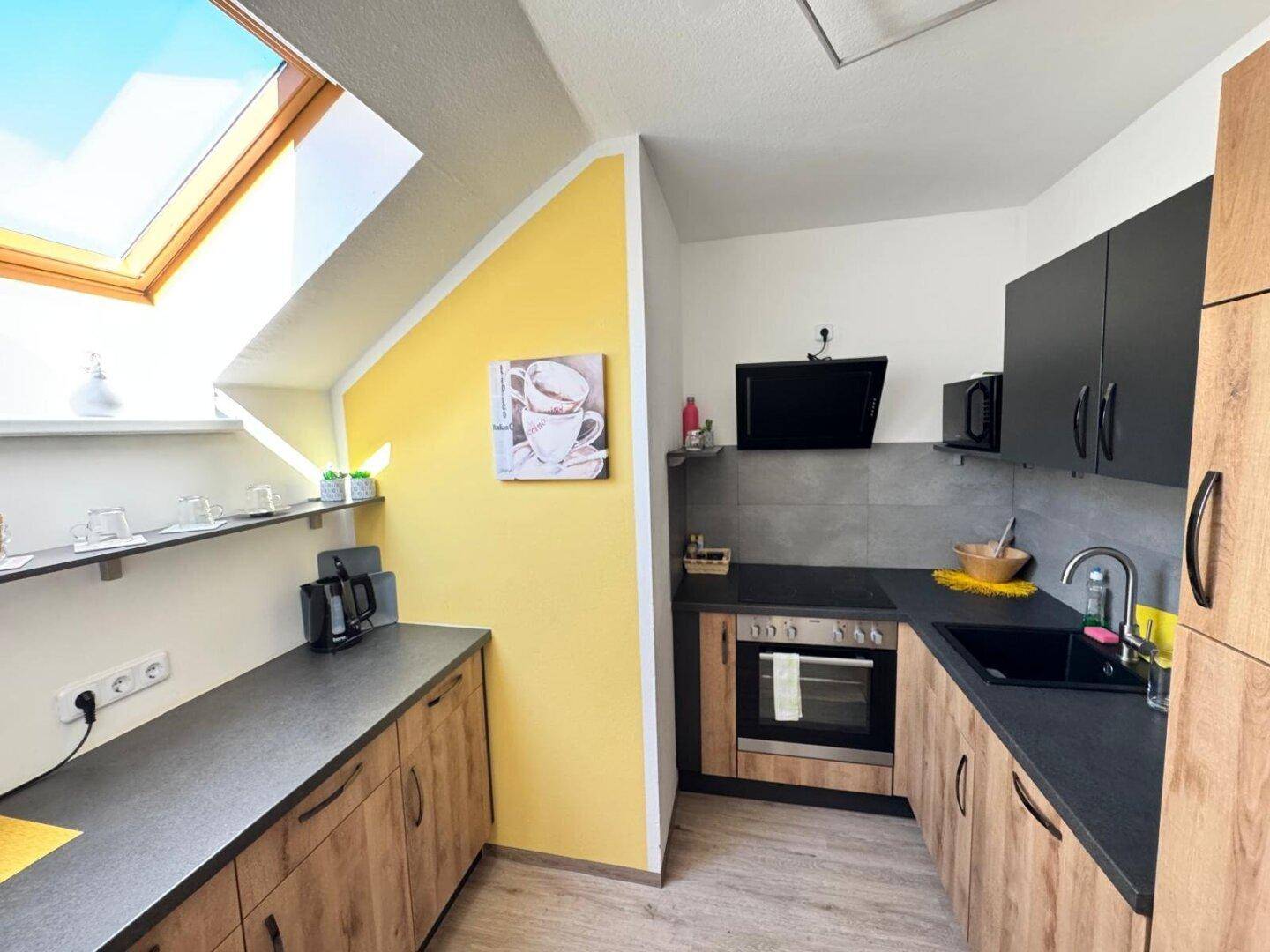 Moderne Küche mit Holzfronten, dunkler Arbeitsplatte und Dachfenster für viel Licht.