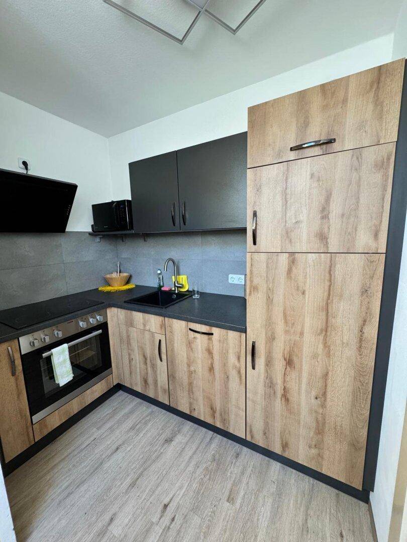 Funktionale Küche mit Holz- und dunklen Schränken, integrierten Geräten und Laminatboden.
