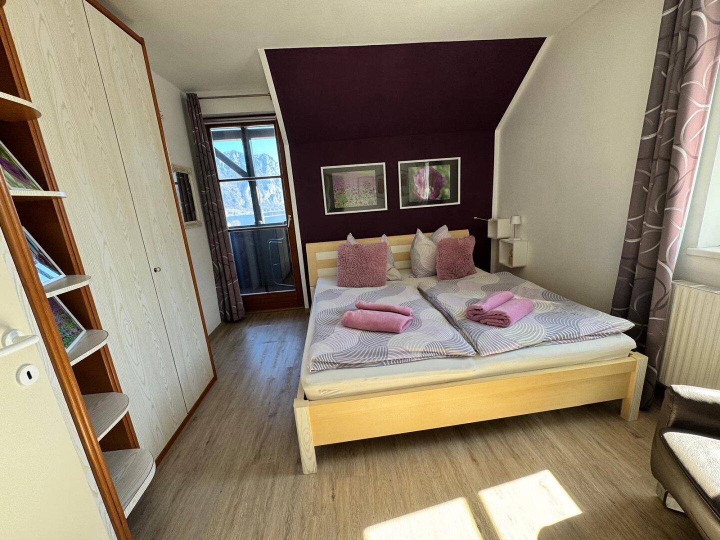 Gemütliches Schlafzimmer mit Doppelbett, lila Akzentwand und Zugang zum Balkon.