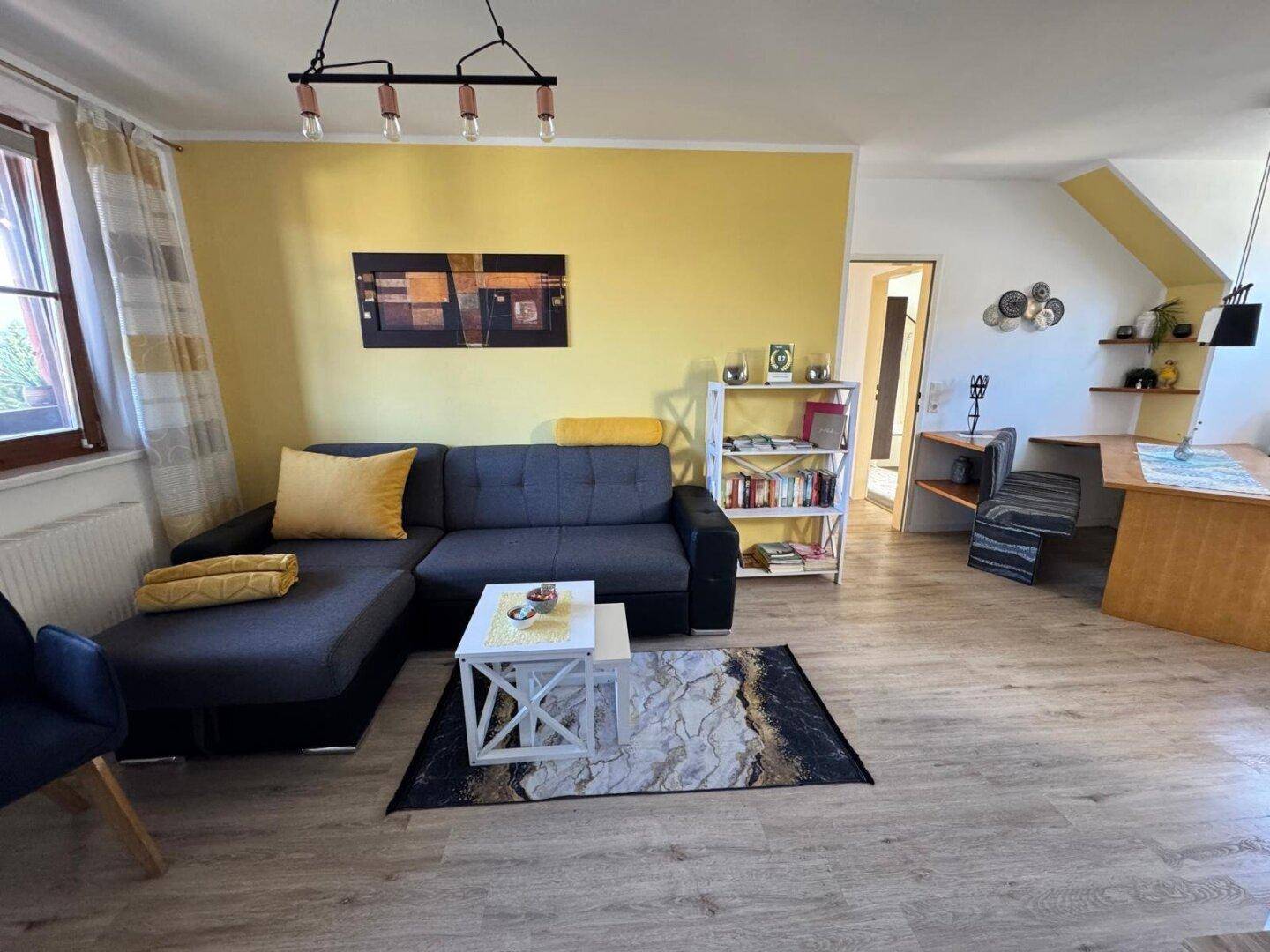 Helles Wohnzimmer mit Ecksofa, gelber Akzentwand und modernem Couchtisch.
