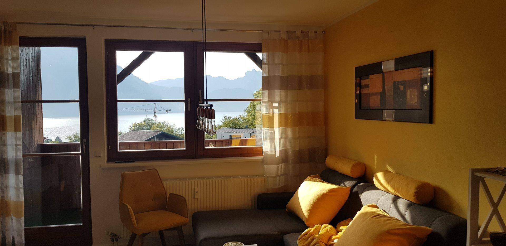 Lichtdurchflutetes Wohnzimmer mit Seeblick, gelben Akzenten und warmem Sonnenlicht.