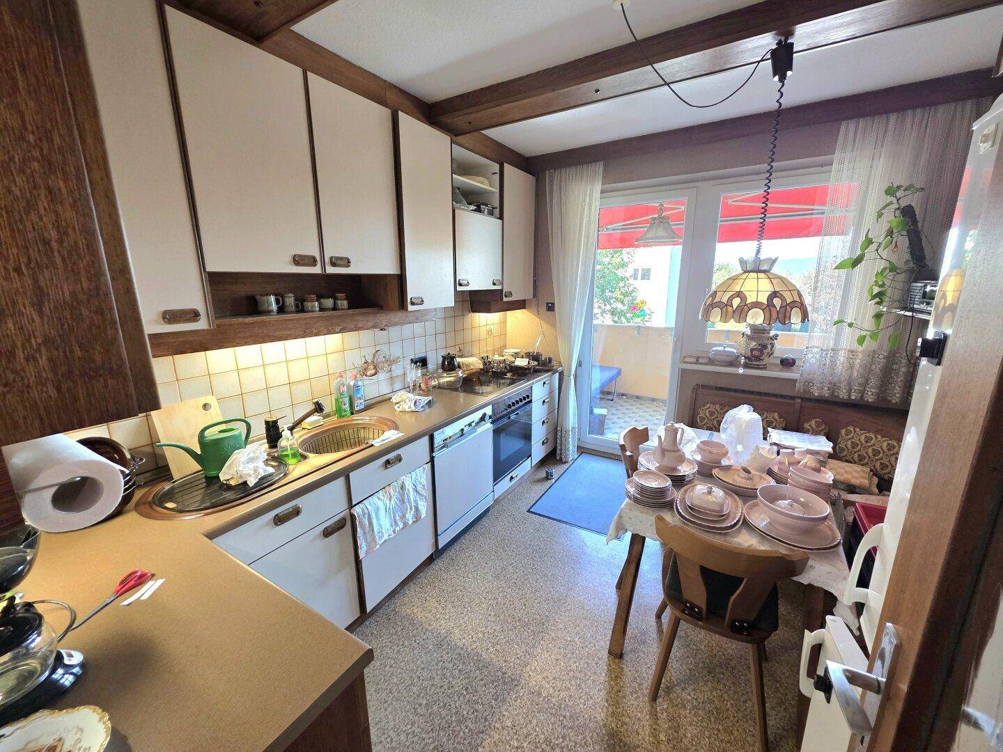 Funktionale Küche mit Essbereich, weißen Schränken, Holzbalken und Zugang zum Balkon.