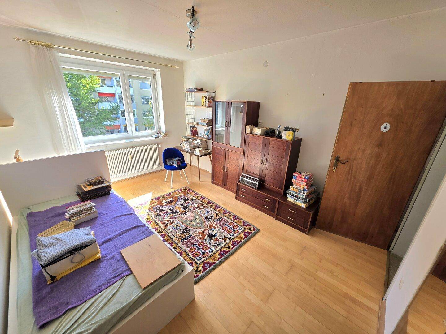 Helles Schlafzimmer mit Holzboden, Teppich und Fenster mit Blick auf die Umgebung.
