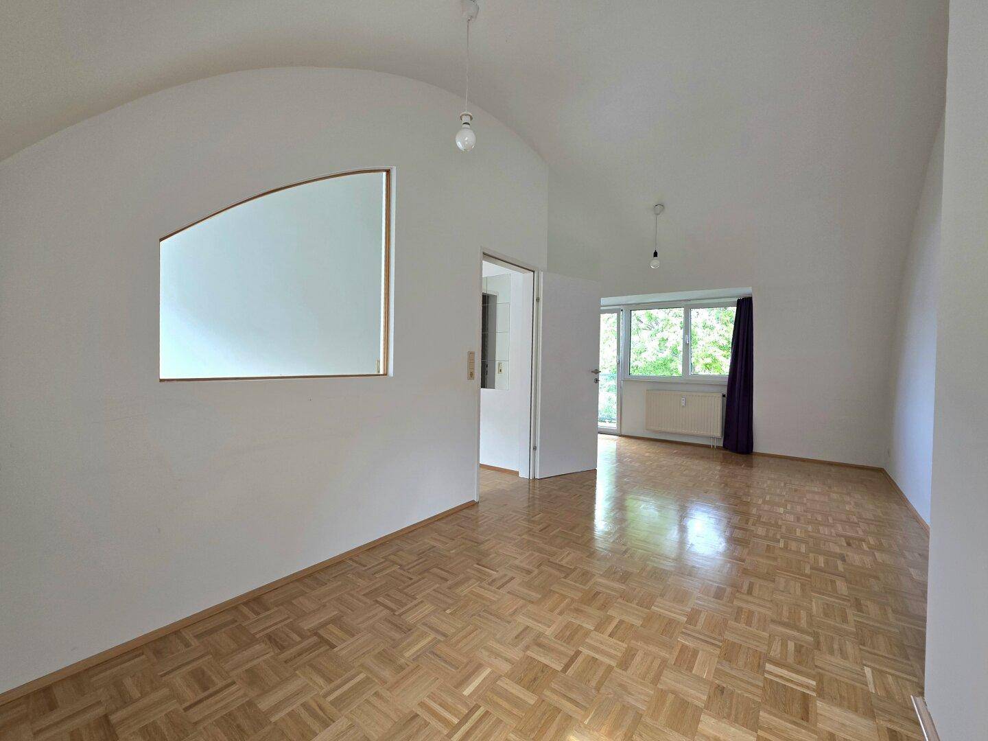 Geräumiger Wohnbereich mit Parkettboden, gewölbter Decke und natürlichem Lichteinfall.