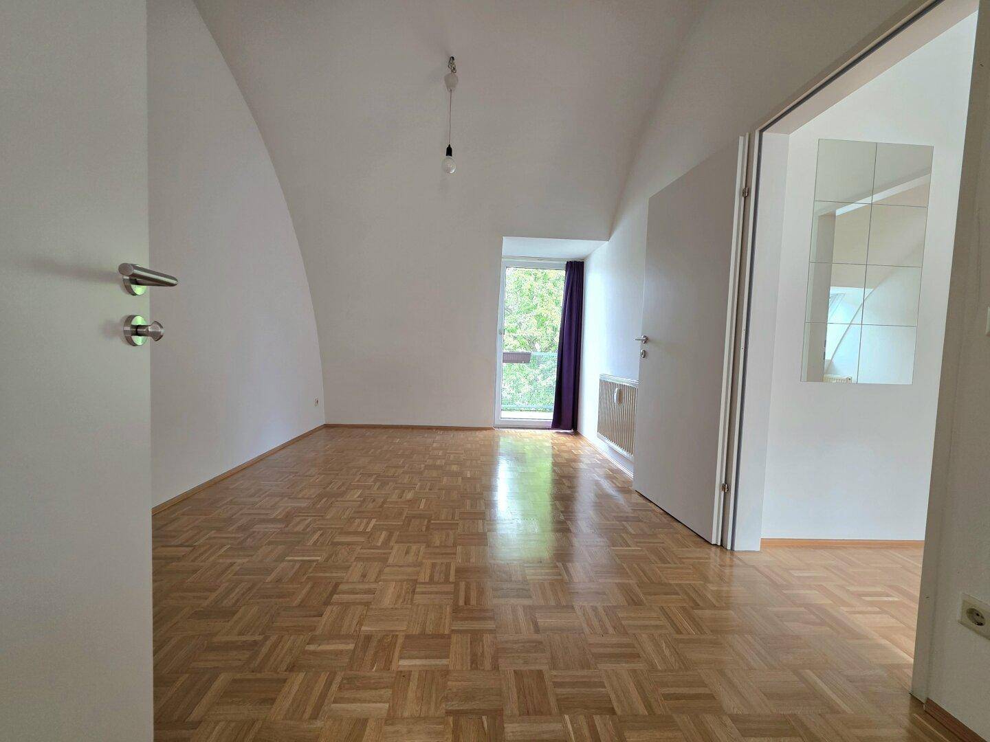 Helles Zimmer mit Parkettboden, gewölbter Decke und Fenster mit Blick ins Grüne.