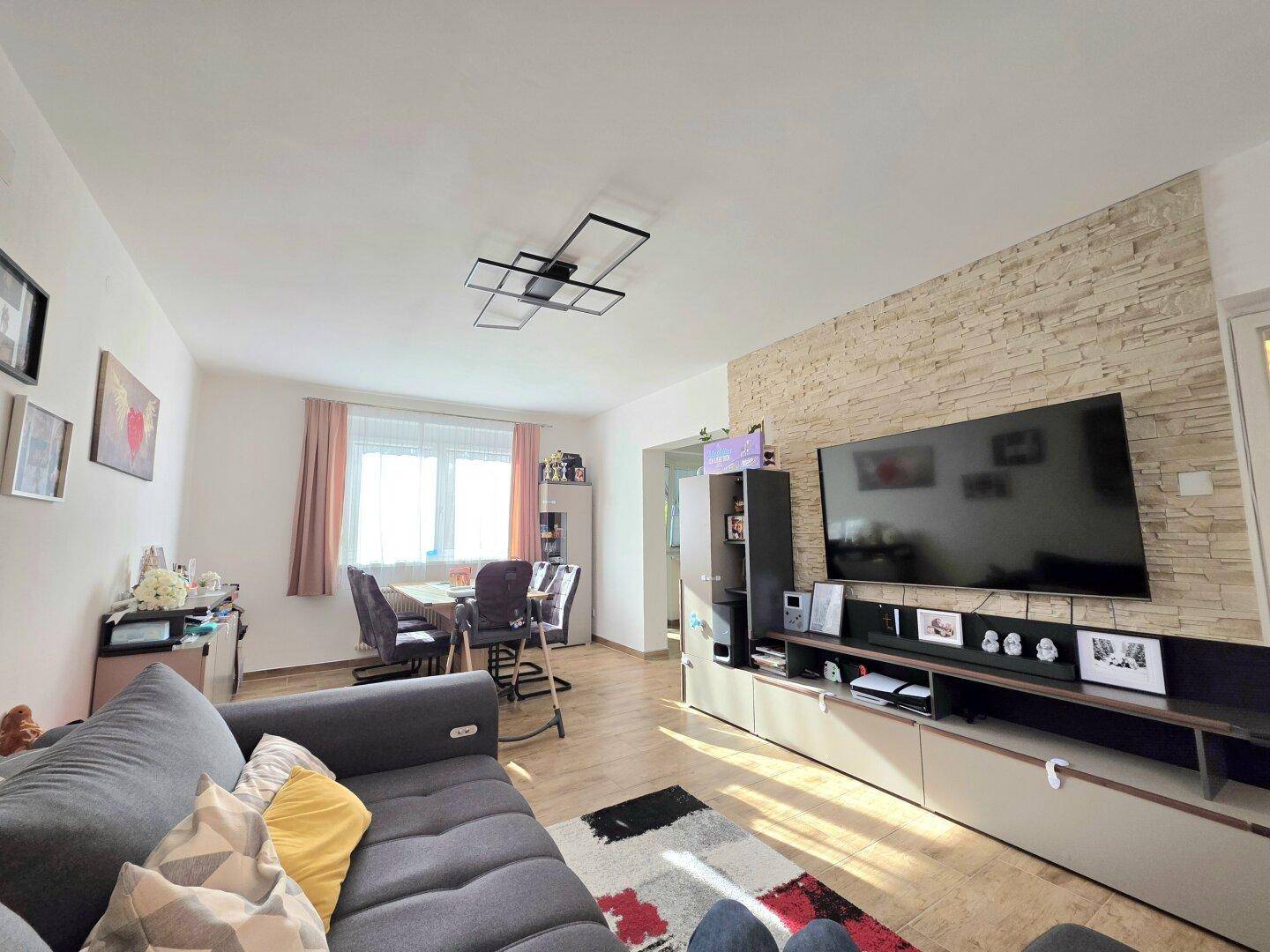 Gemütlicher Wohnbereich mit Steinfassade, großem Fernseher und Essbereich im Hintergrund.