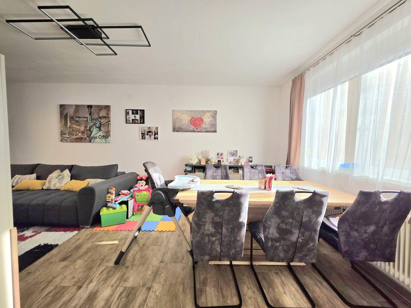 Heller Wohn- und Essbereich mit großem Esstisch, Sofa und Spielbereich für Kinder.