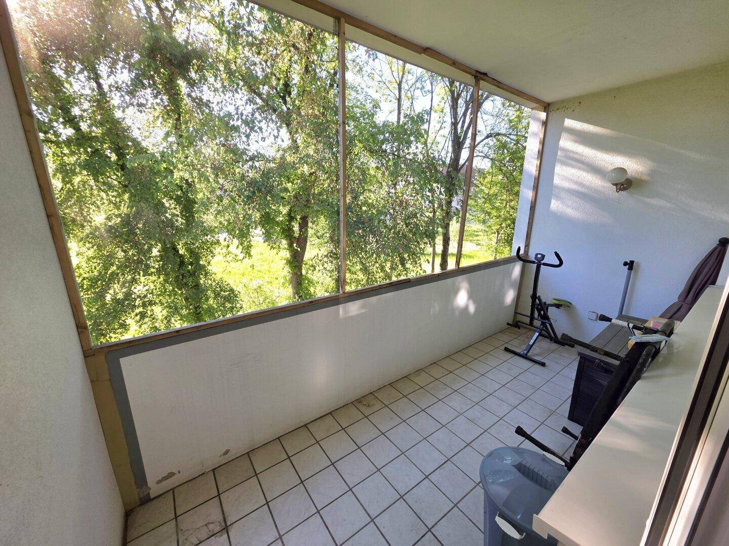 Geräumiger Balkon mit Fliesenboden, Fitnessgeräten und weitem Blick ins Grüne.