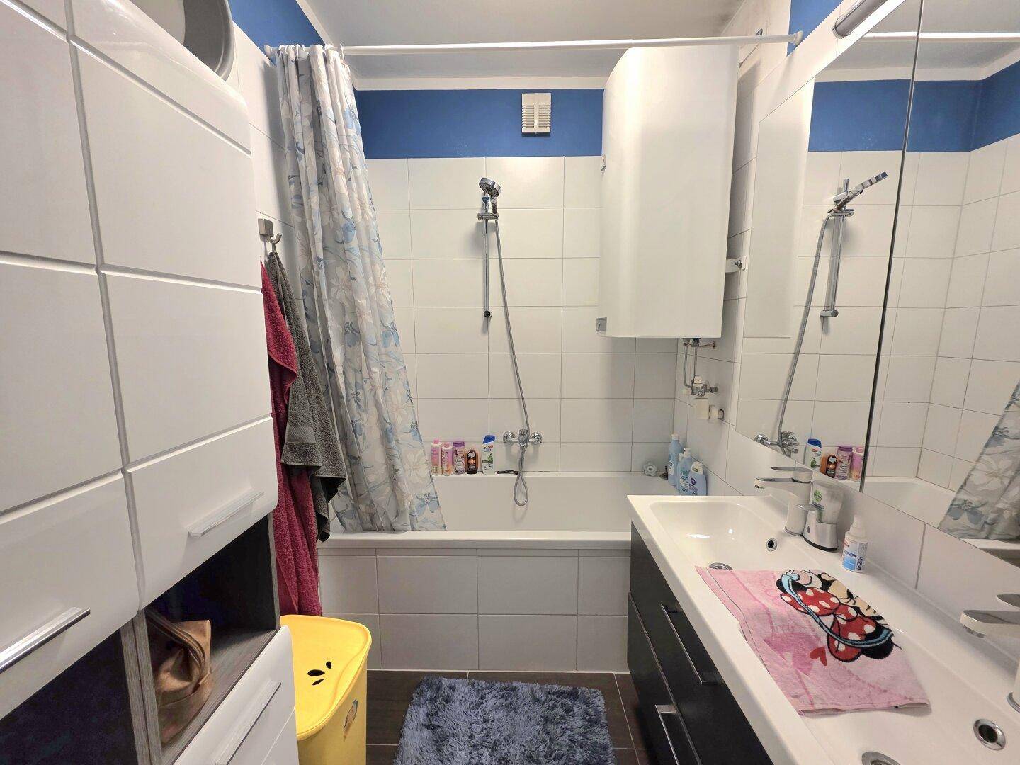 Badezimmer mit Badewanne, Duschvorhang, Waschbecken und Spiegelschrank.