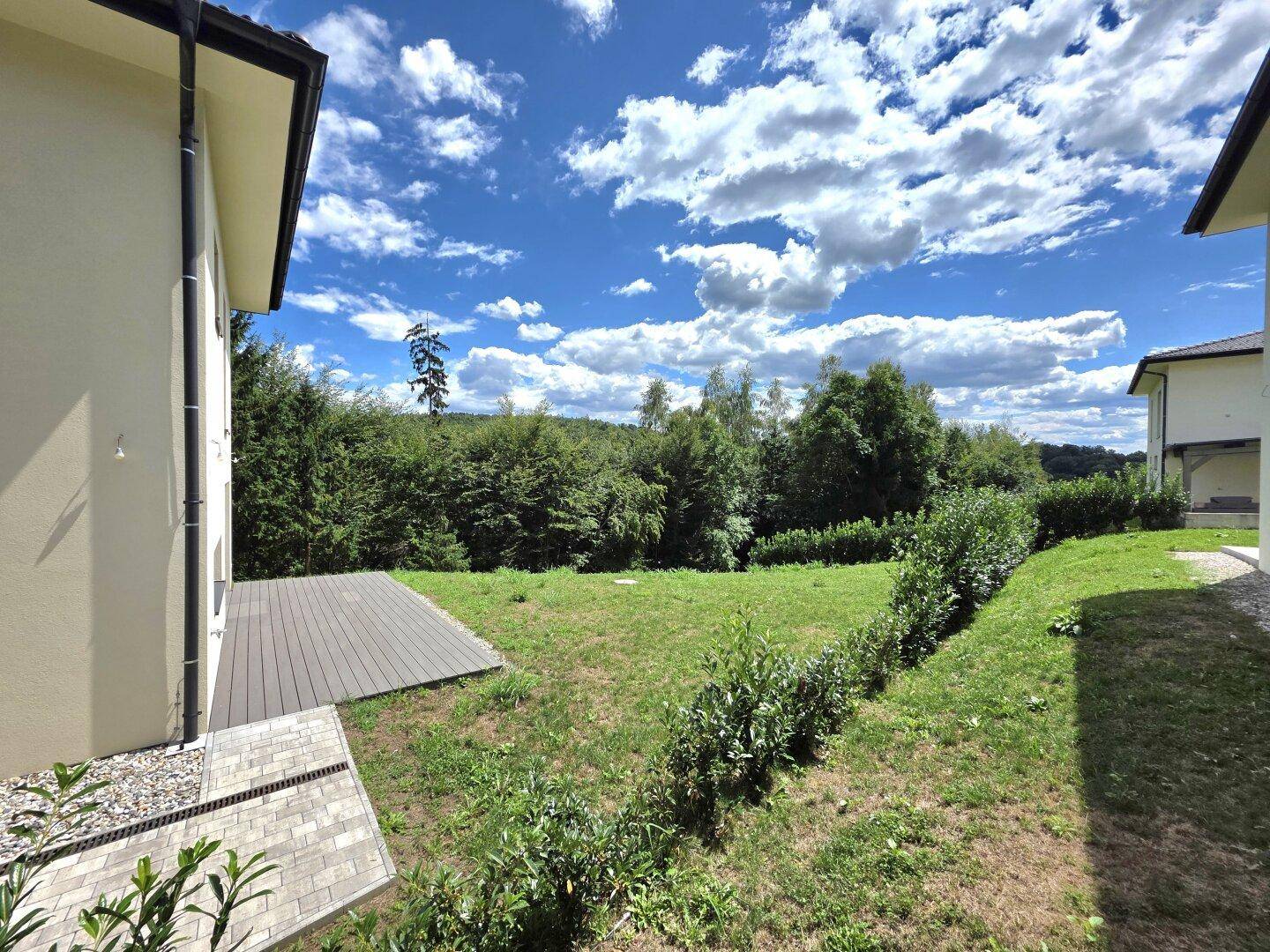 Großer Gartenbereich mit Rasenfläche und Hecken, umgeben von Bäumen unter blauem Himmel.