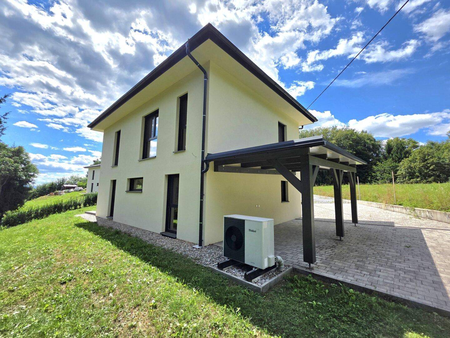 Rückansicht des modernen Hauses mit Carport und Wärmepumpe, umgeben von viel Grün.