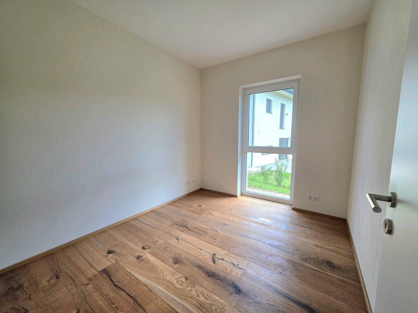 Helles Schlafzimmer mit Holzboden und großem Fenster, das viel Tageslicht hereinlässt.