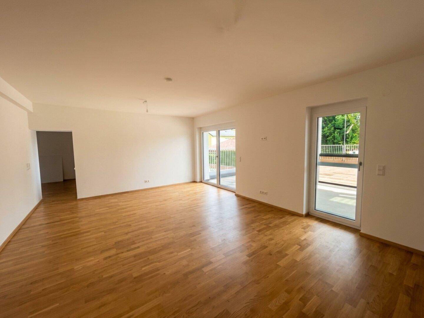 Geräumiges Wohnzimmer mit Parkettboden und direktem Zugang zu einem sonnigen Balkon.