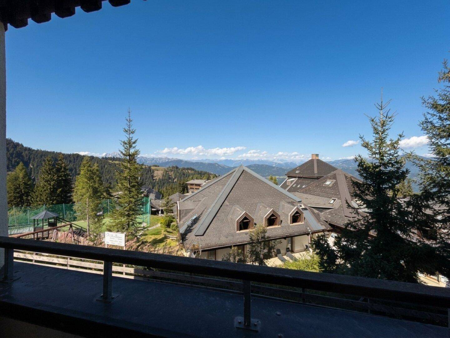 Panoramablick vom Balkon auf die umliegende Berglandschaft, Wälder und weitere Gebäude unter blauem Himmel.