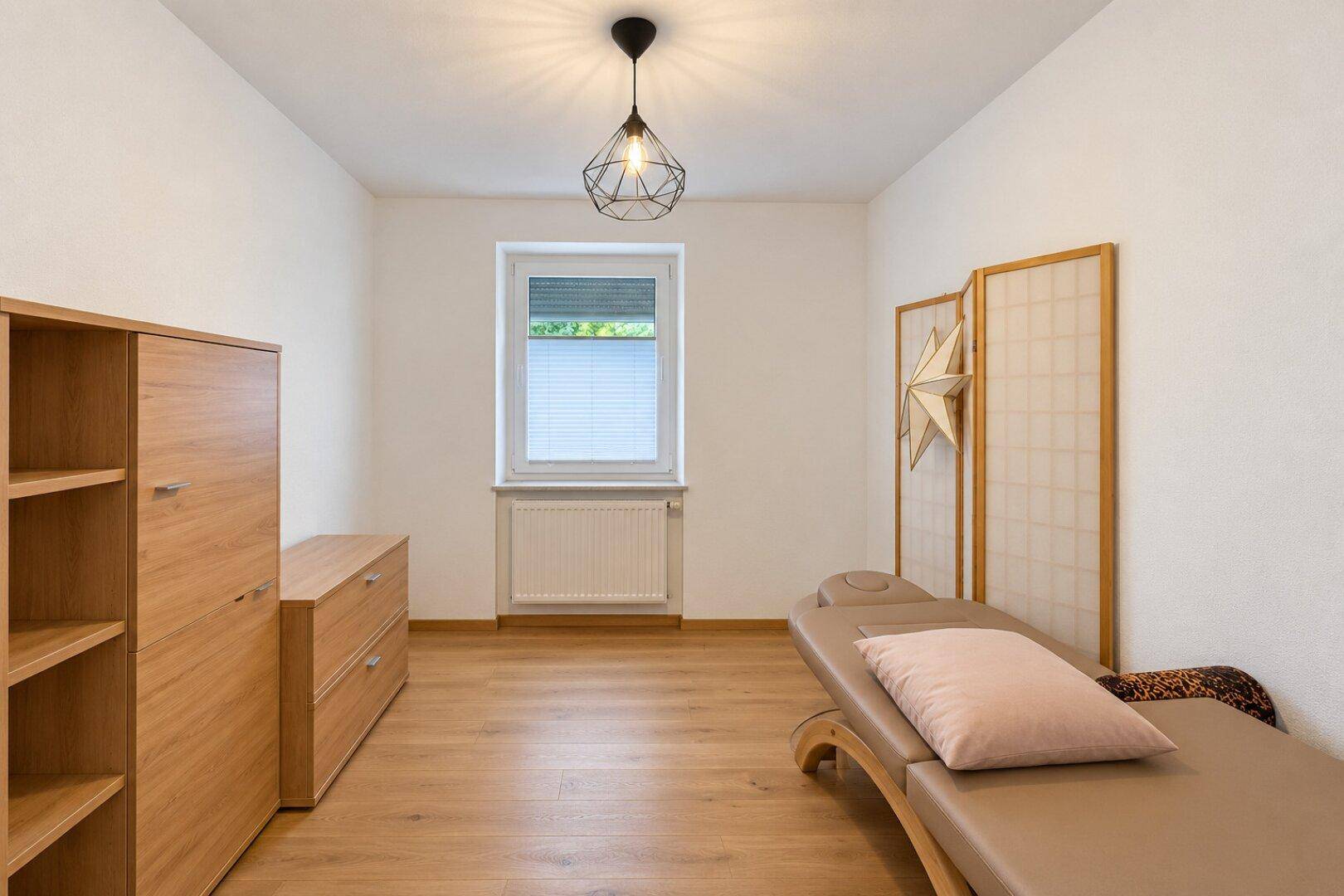 Vielseitiger Raum mit Holzboden, einem Fenster und schlichten Holzmöbeln, ideal als Gästezimmer.