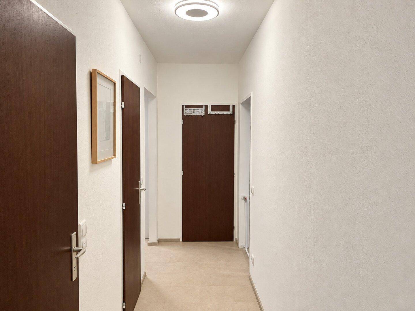 Langer, heller Flur mit mehreren Türen und einem modernen Deckenlicht.