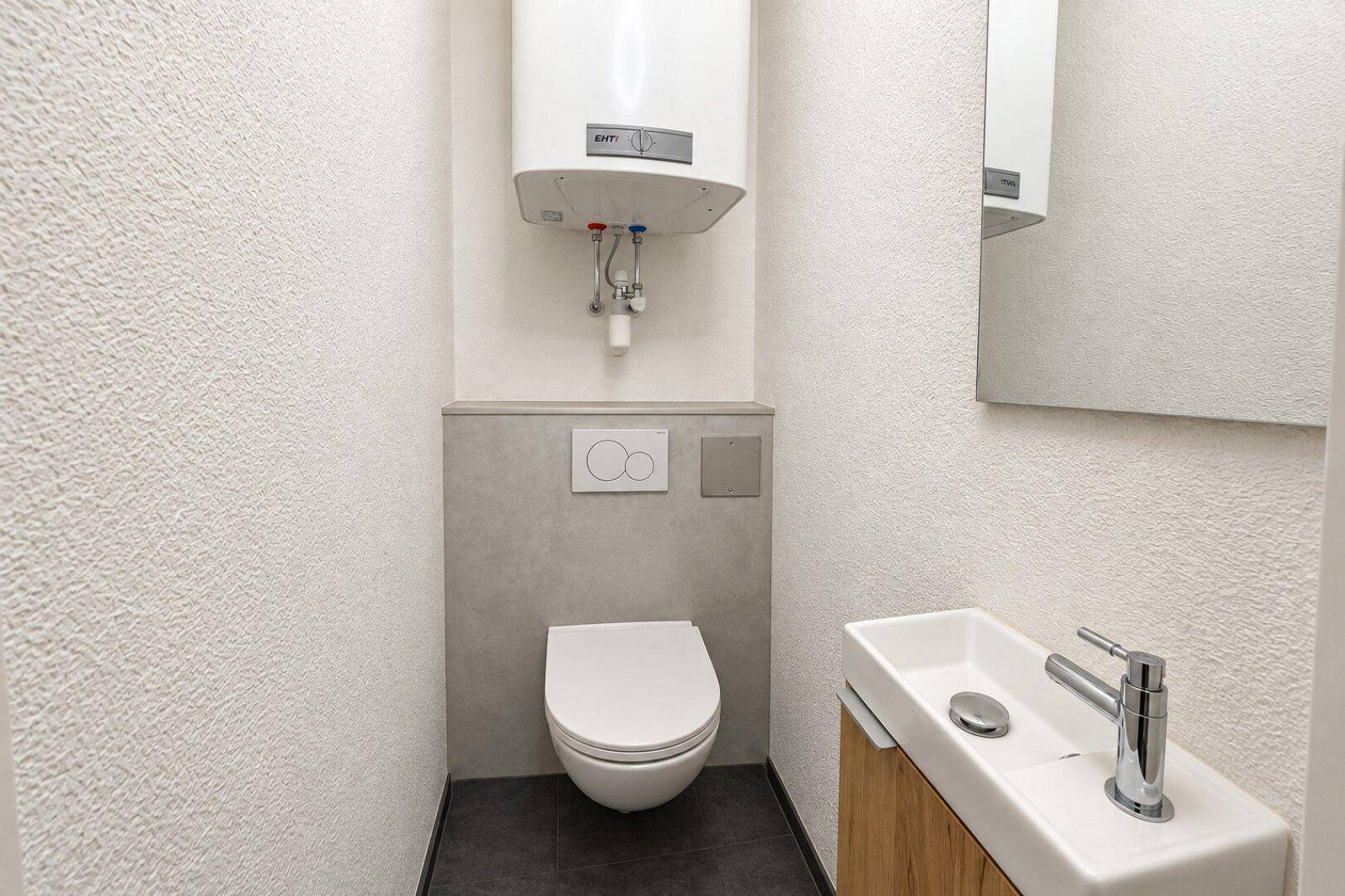 Kleines Gäste-WC mit wandhängendem WC, kleinem Waschbecken und Boiler.