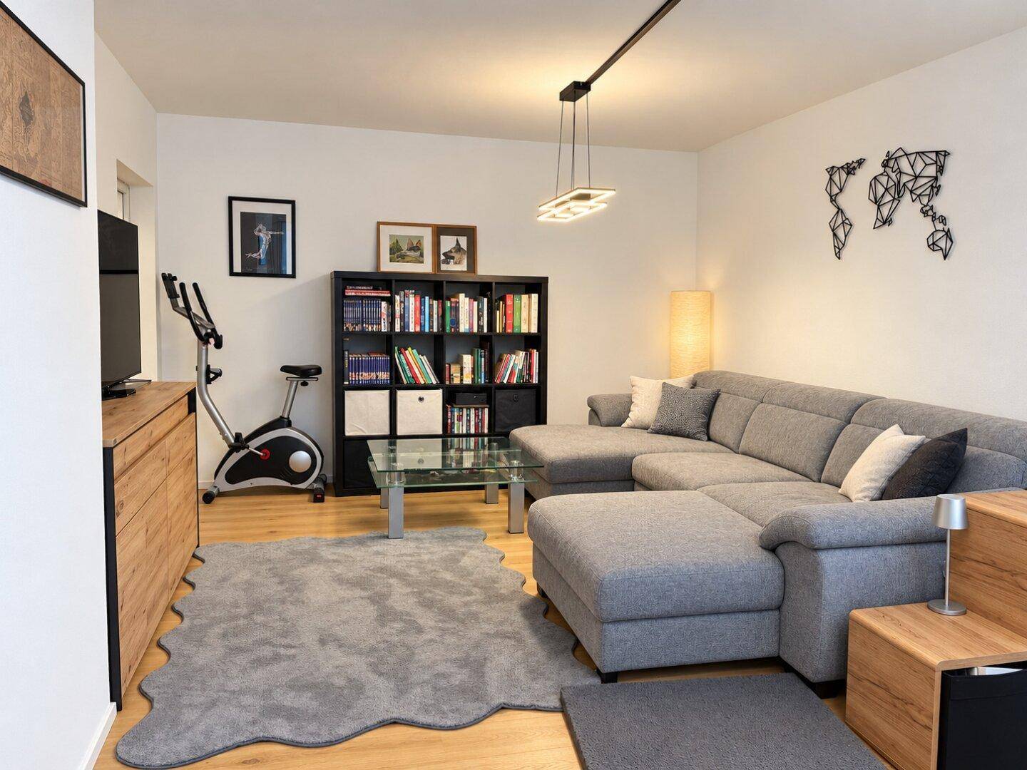 Geräumiges Wohnzimmer mit Sofa, Bücherregal und einem Heimtrainer für sportliche Aktivitäten.