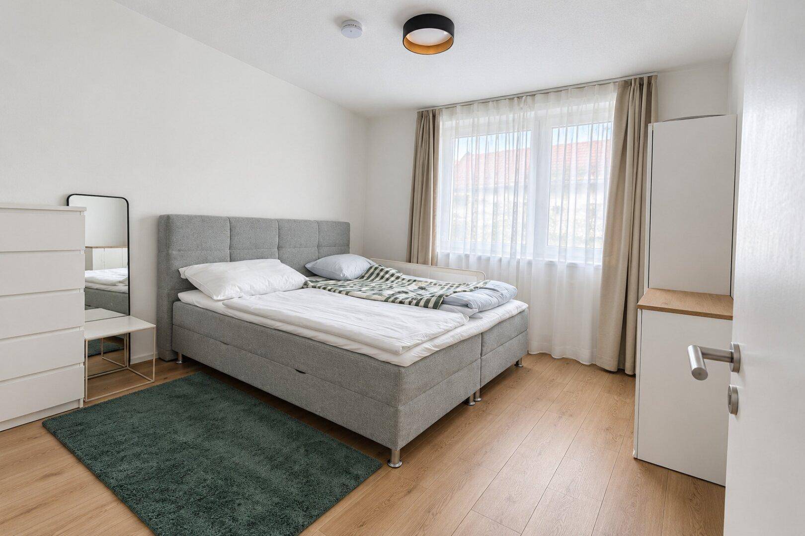 Gemütliches Schlafzimmer mit Doppelbett, Holzfußboden und viel Tageslicht.