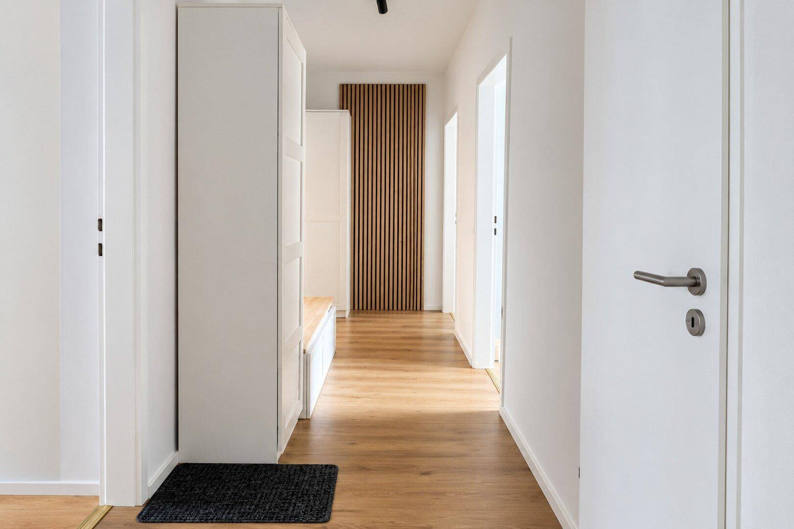 Heller Flur mit Holzfußboden, weißen Schränken und moderner Wandverkleidung.