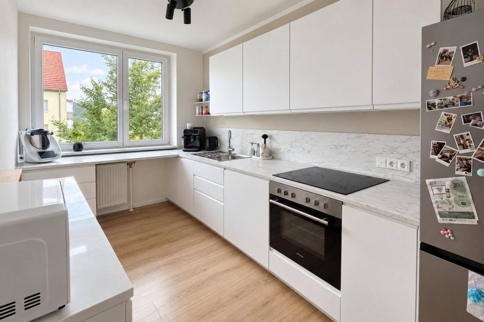 Moderne Einbauküche mit weißen Fronten, Induktionskochfeld und Fenster.