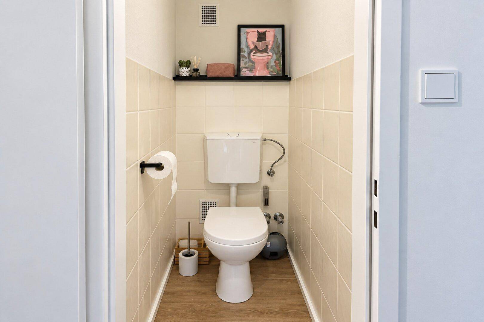 Separates WC mit Toilette, Fliesen an den Wänden und Holzoptikboden.