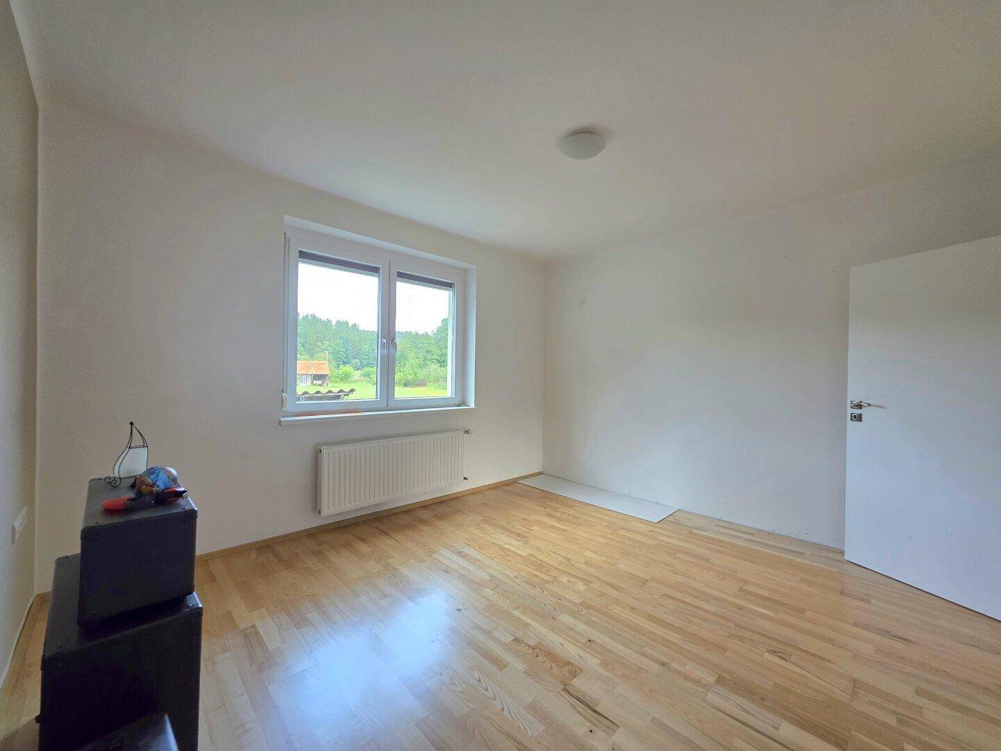 Schlafzimmer mit hellem Parkettboden und Fenster, das viel Tageslicht hereinlässt.