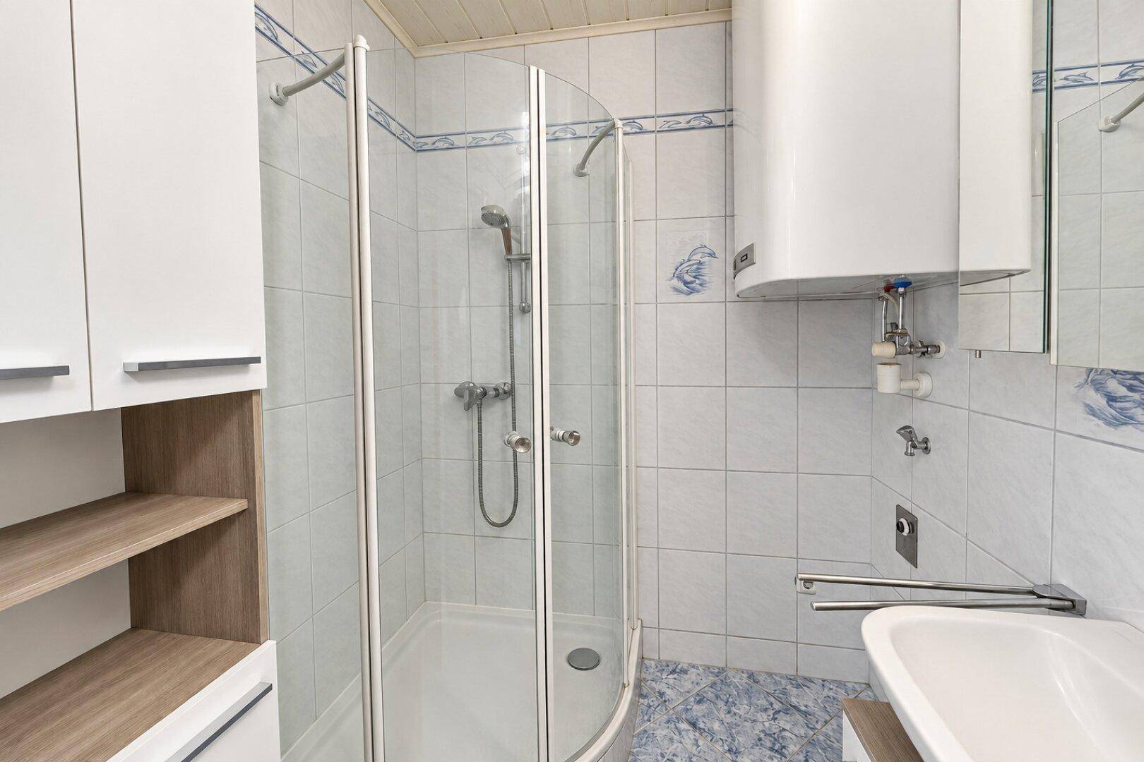Badezimmer mit Eckdusche, weiß-blauen Fliesen und einem Warmwasserboiler.