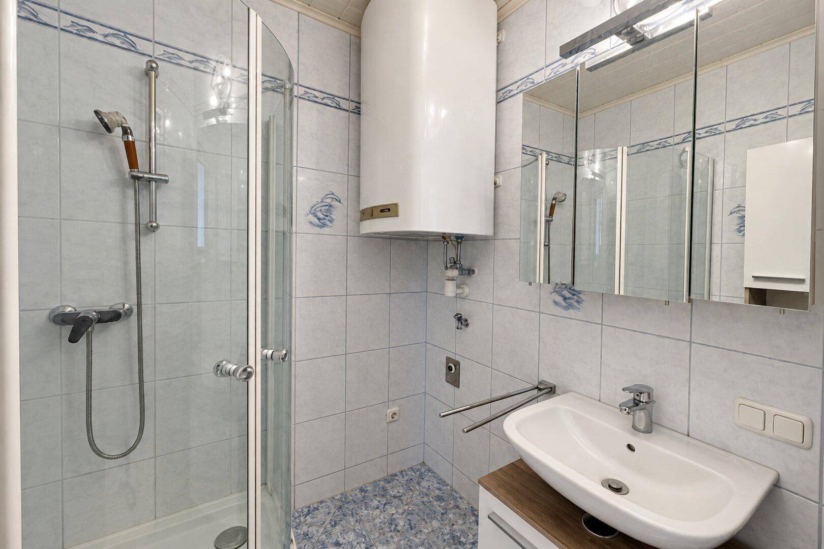 Badezimmer mit Eckdusche, Waschbecken, Spiegelschrank und Warmwasserboiler.