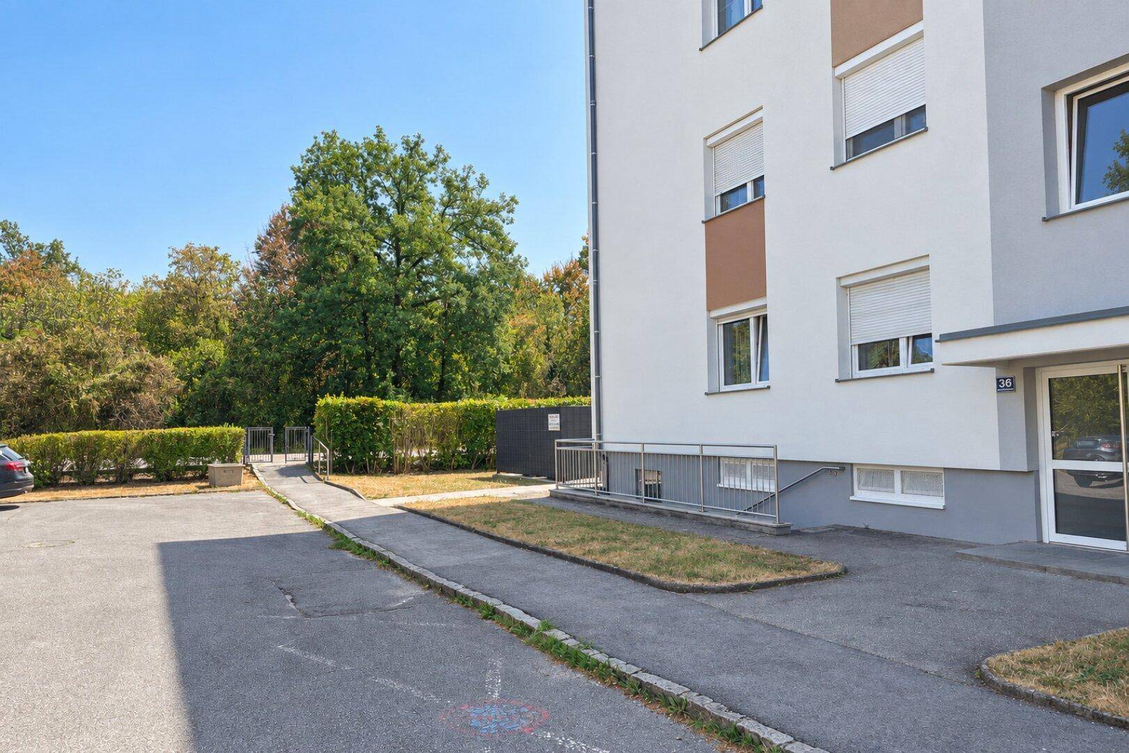 Seitenansicht eines modernen Wohngebäudes mit Parkplätzen und grüner Hecke.