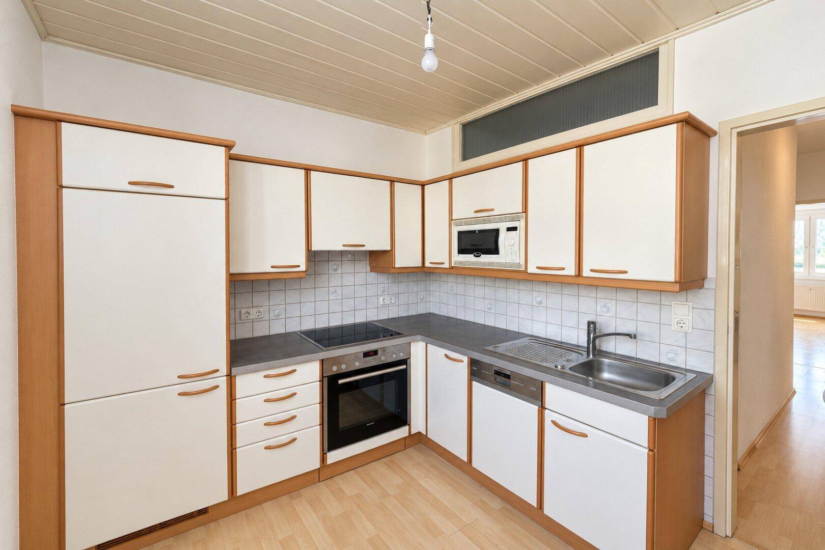 Funktionale Küche mit hellen Holzschränken, integrierten Geräten und Fliesenrückwand.
