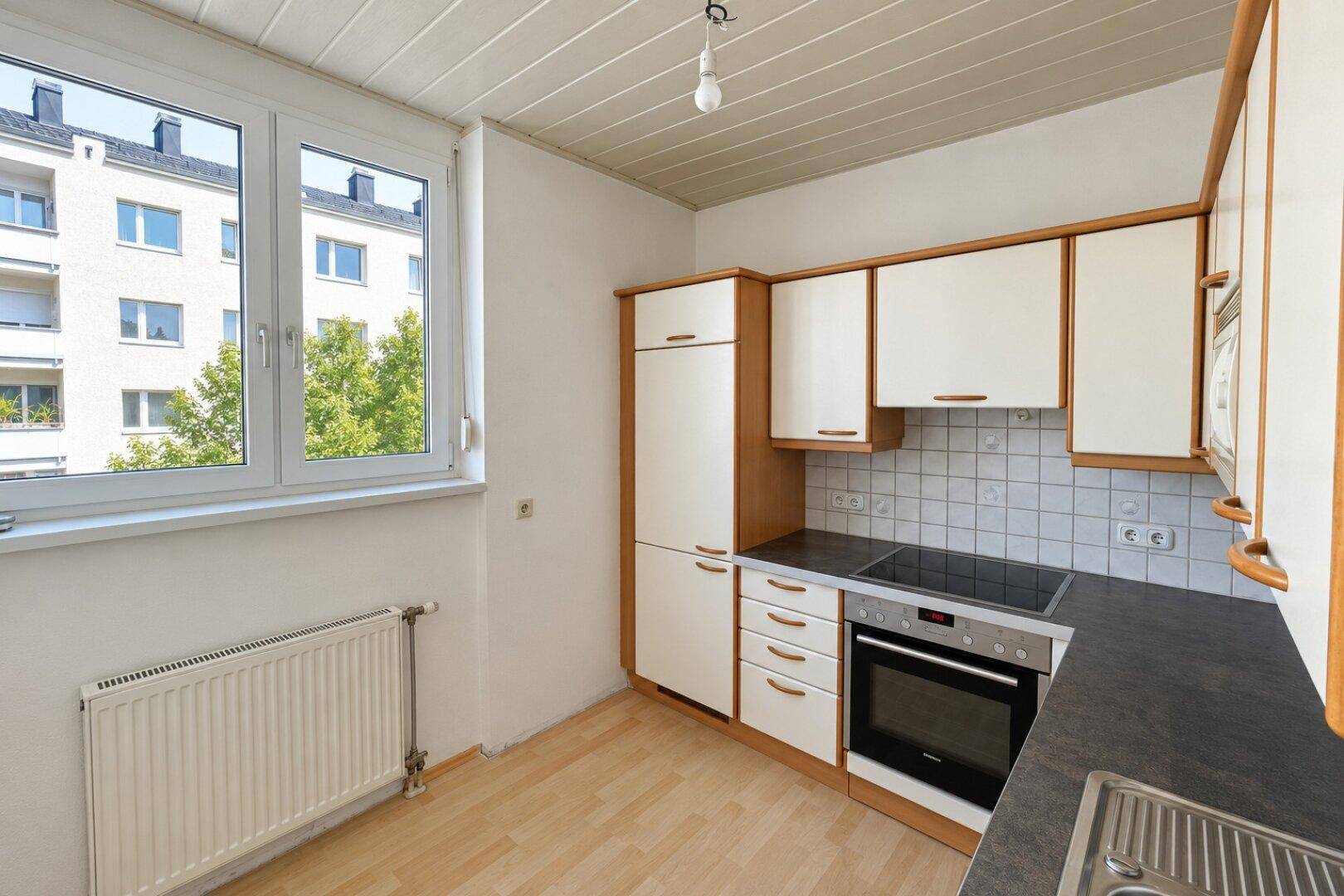 Helle Küche mit Holzschränken, integrierten Geräten und Blick auf umliegende Gebäude.